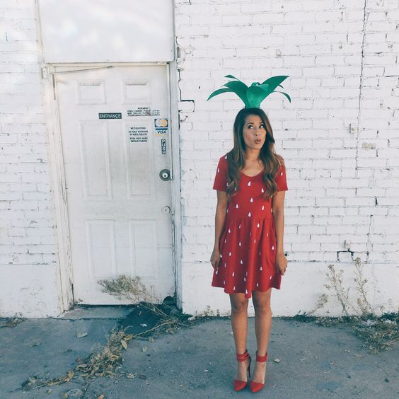 a woman standing in front of a white door wearing a red dress with a green pine on it's head