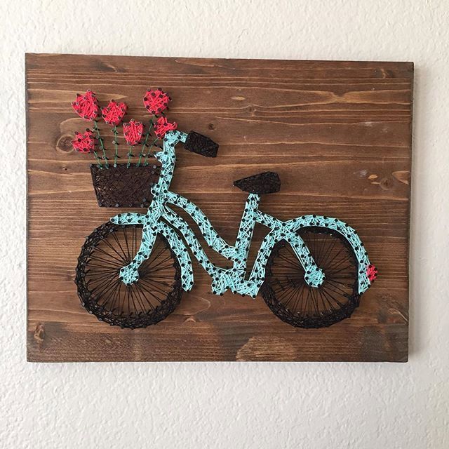 a wooden sign with a bicycle and flowers on the front, hanging on a wall