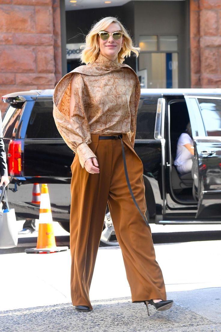 a woman in brown pants and heels is seen walking down the street
