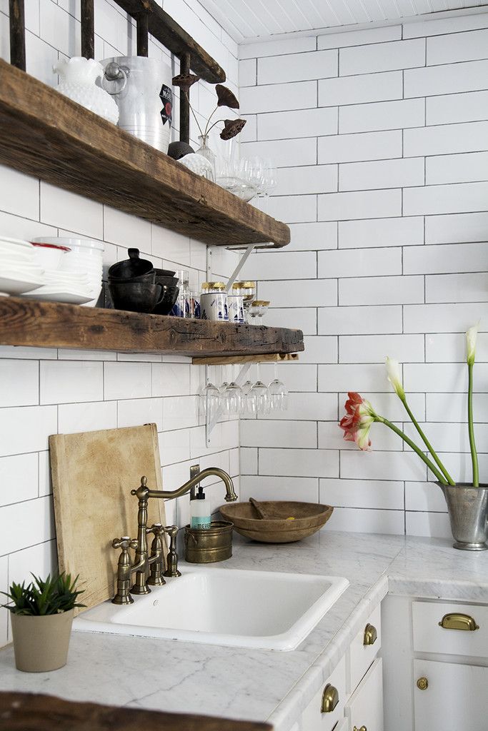 a white kitchen with wooden shelves and open shelving above the sink is filled with dishes