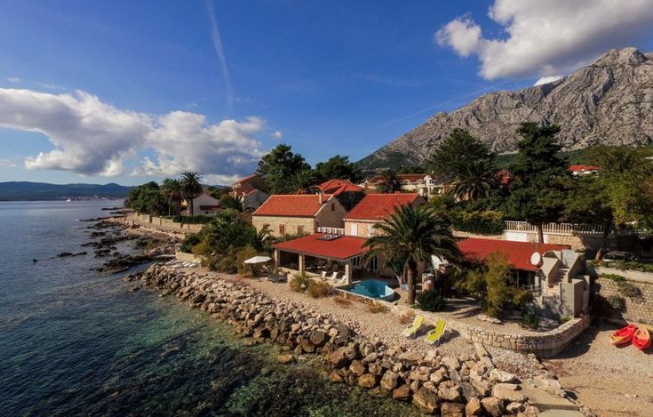 an aerial view of a house on the shore with mountains in the background and blue sky