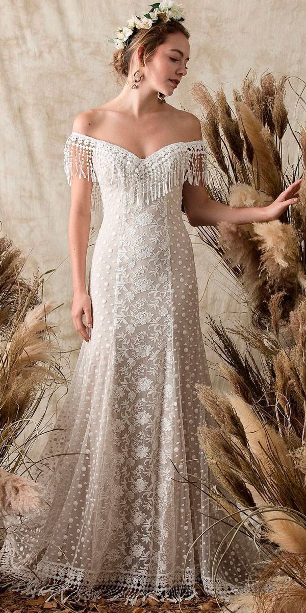 a woman in a white dress standing next to some tall grass and dried plants with her hands on her hips