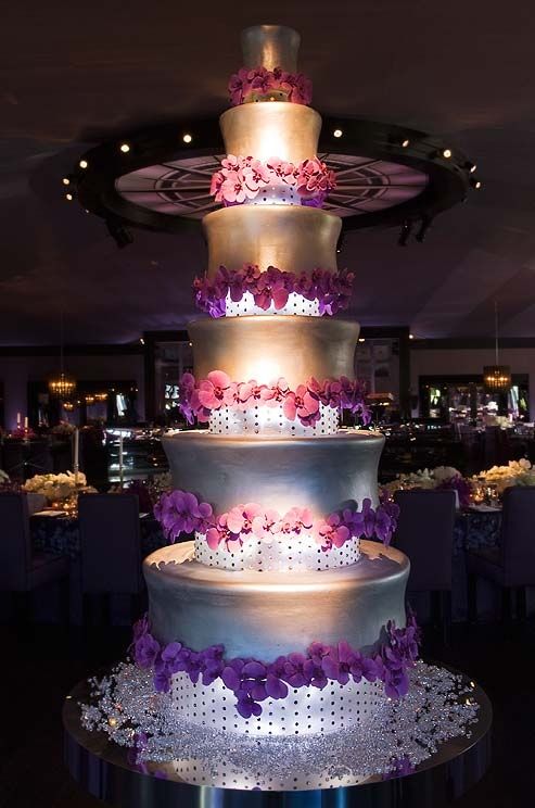 A six tiered cake covered in silver fondant is decorated