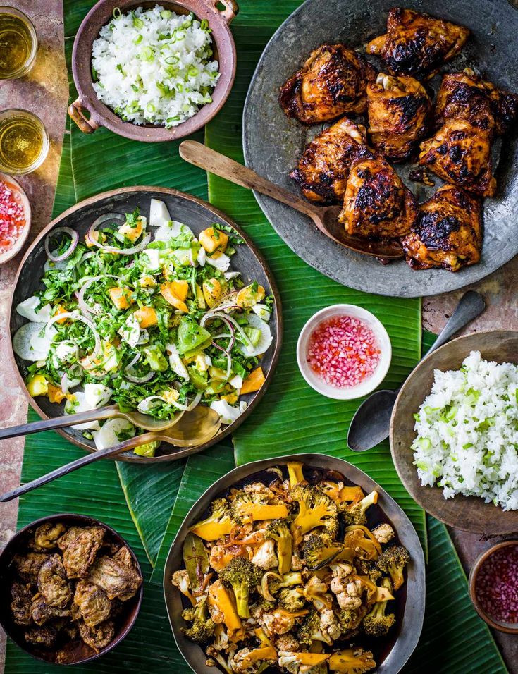 an overhead view of various food dishes on a table with green leaves and wine glasses