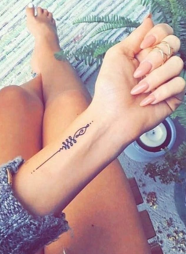 a woman with a tattoo on her arm sitting next to a potted fern plant