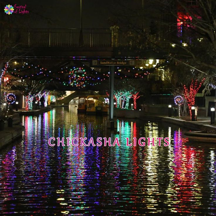 the lights are reflecting in the water on the canal at christmas time and there is a boat going