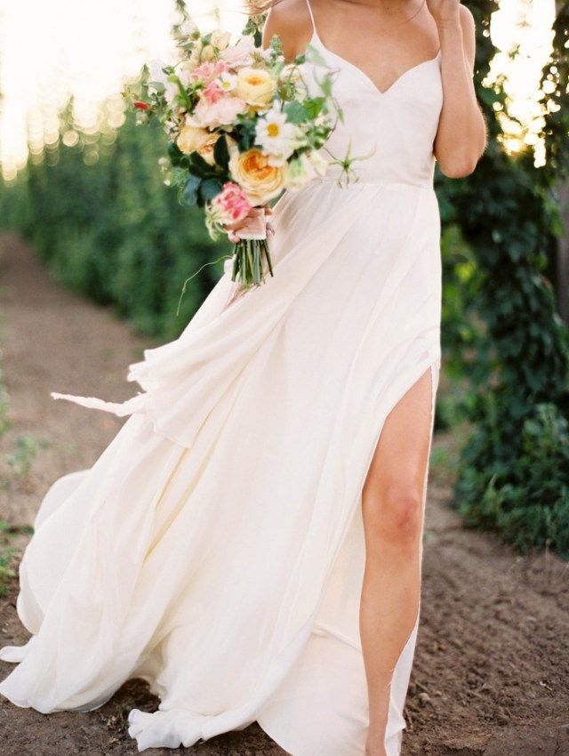 a woman in a white dress is holding a bouquet and talking on her cell phone