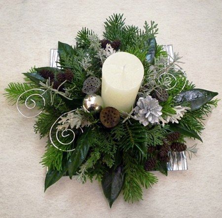 a white candle surrounded by greenery and pine cones