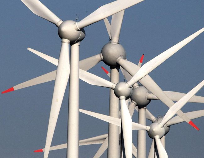 many white wind turbines with red arrows on them against a blue and gray cloudy sky