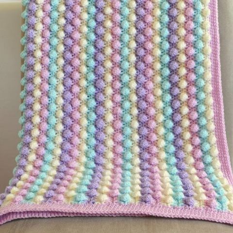 a crocheted blanket sitting on top of a couch next to a white pillow