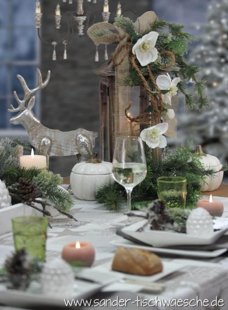 the table is set for christmas dinner with white flowers and greenery, candles and deer figurines