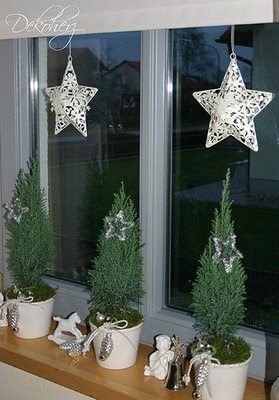 two white stars hanging from the side of a window sill next to potted plants