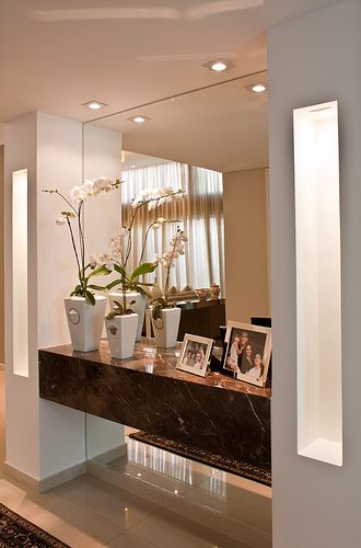 flowers and pictures are sitting on a table in front of a mirror with lights above it