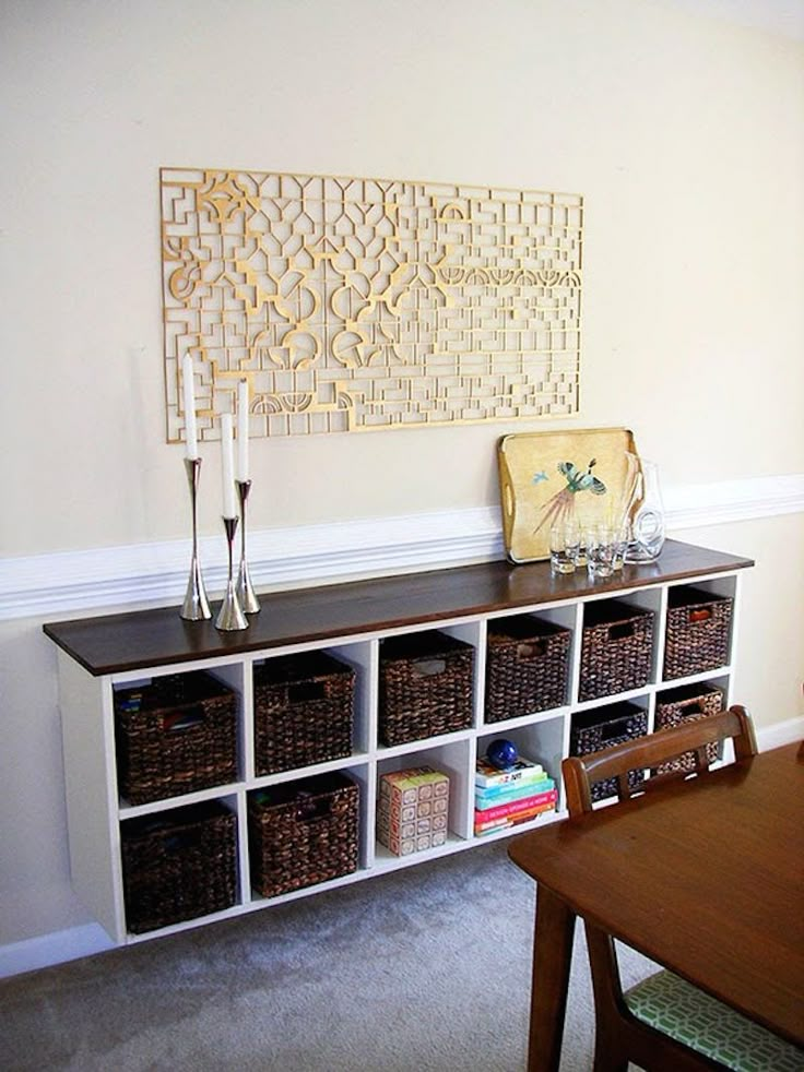 a shelf with baskets and candles on it next to a wall mounted art piece in a dining room