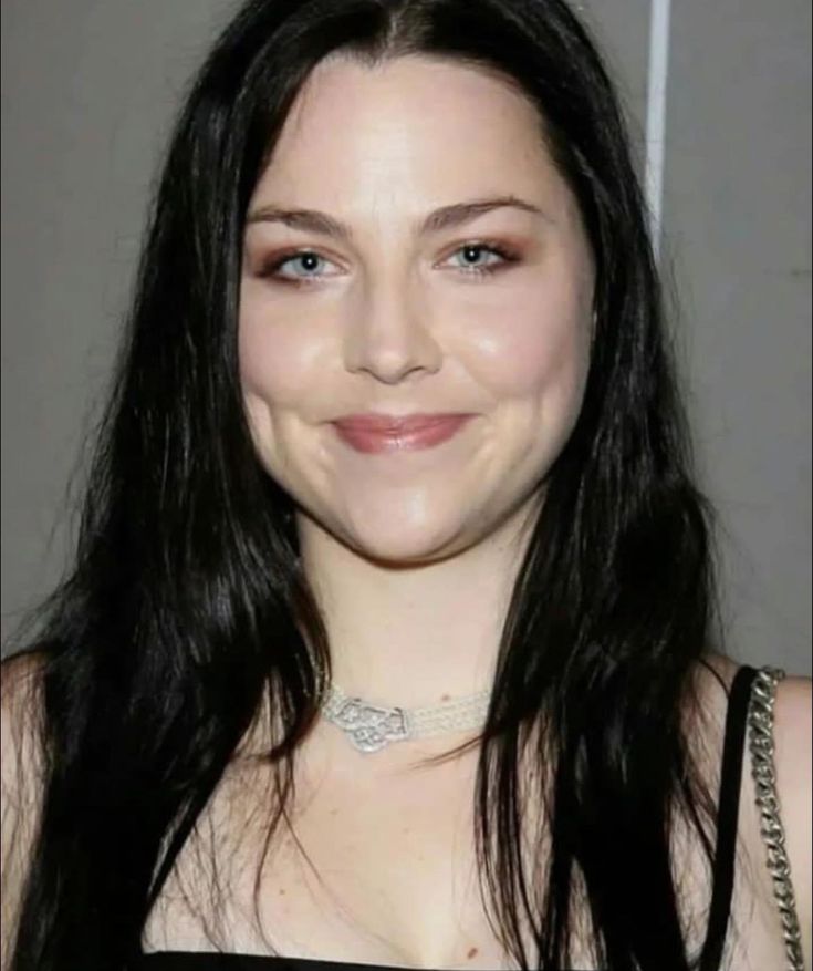 a woman with long black hair smiling at the camera and wearing a choker ...