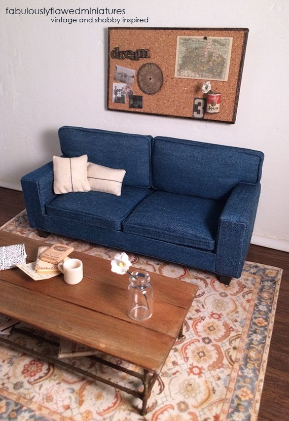 a living room with a blue couch, coffee table and cork board on the wall