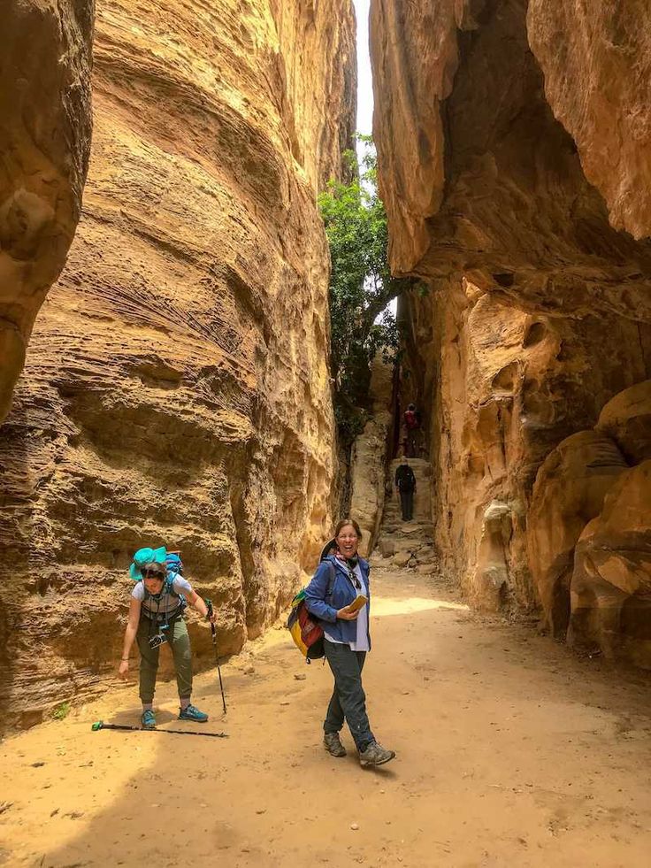 This may contain: two people hiking through a narrow canyon in the desert