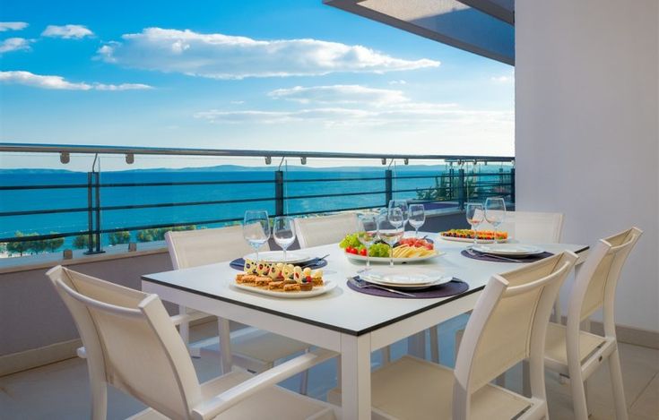 a table with plates of food and glasses on it in front of a balcony overlooking the ocean