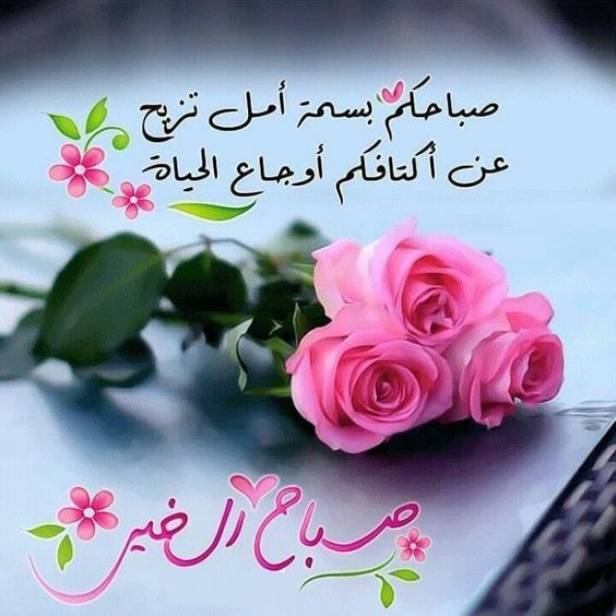 two pink roses sitting on top of a table next to a cell phone with arabic writing