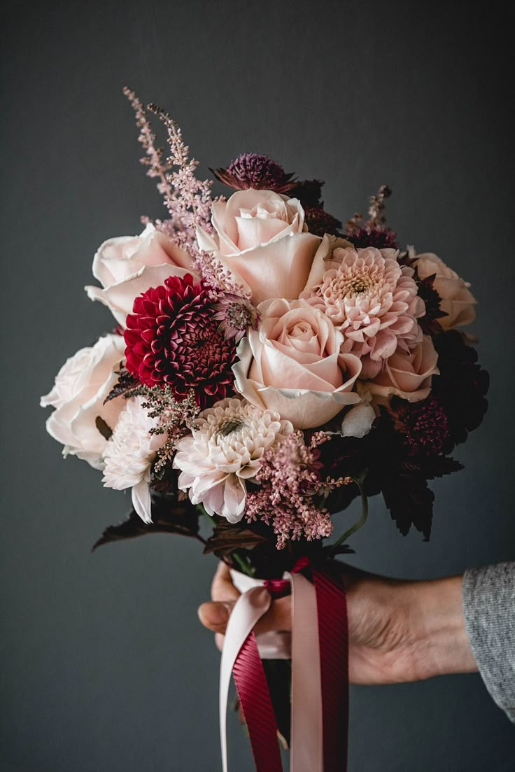 a person holding a bouquet of flowers in their hand with a ribbon around the wrist