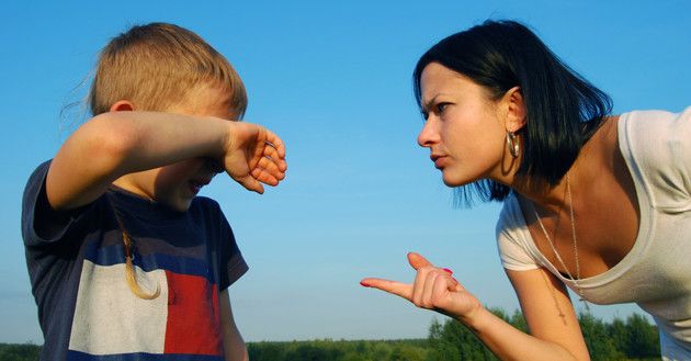 a woman pointing at a boy in the middle of a field with grass and blue sky behind her