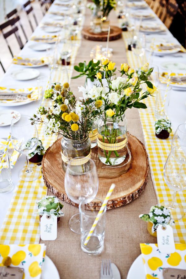 the table is set with yellow and white flowers in mason jar vases on wood slices