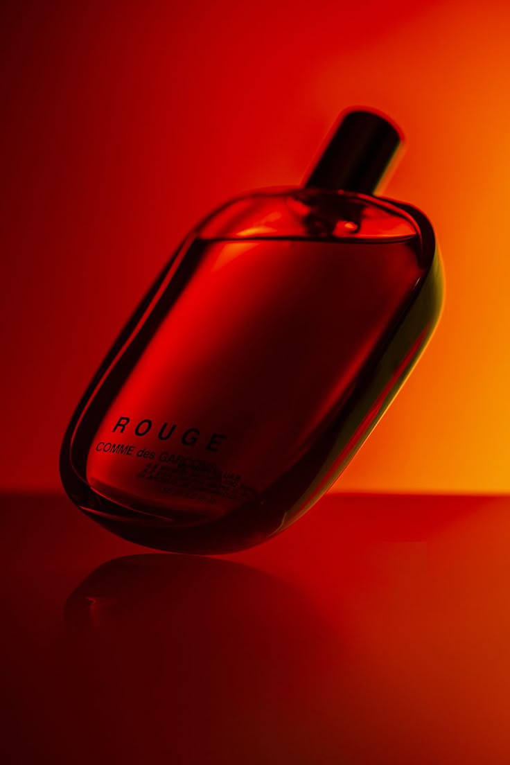 A Bottle Of Cologne Sitting On Top Of A Table Next To An Orange And Red a-bottle-of-cologne-sitting-on-top-of-a-table-next-to-an-orange-and-red