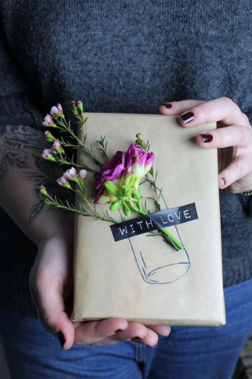 a woman holding a wrapped present with flowers in it's wrapper that says with love