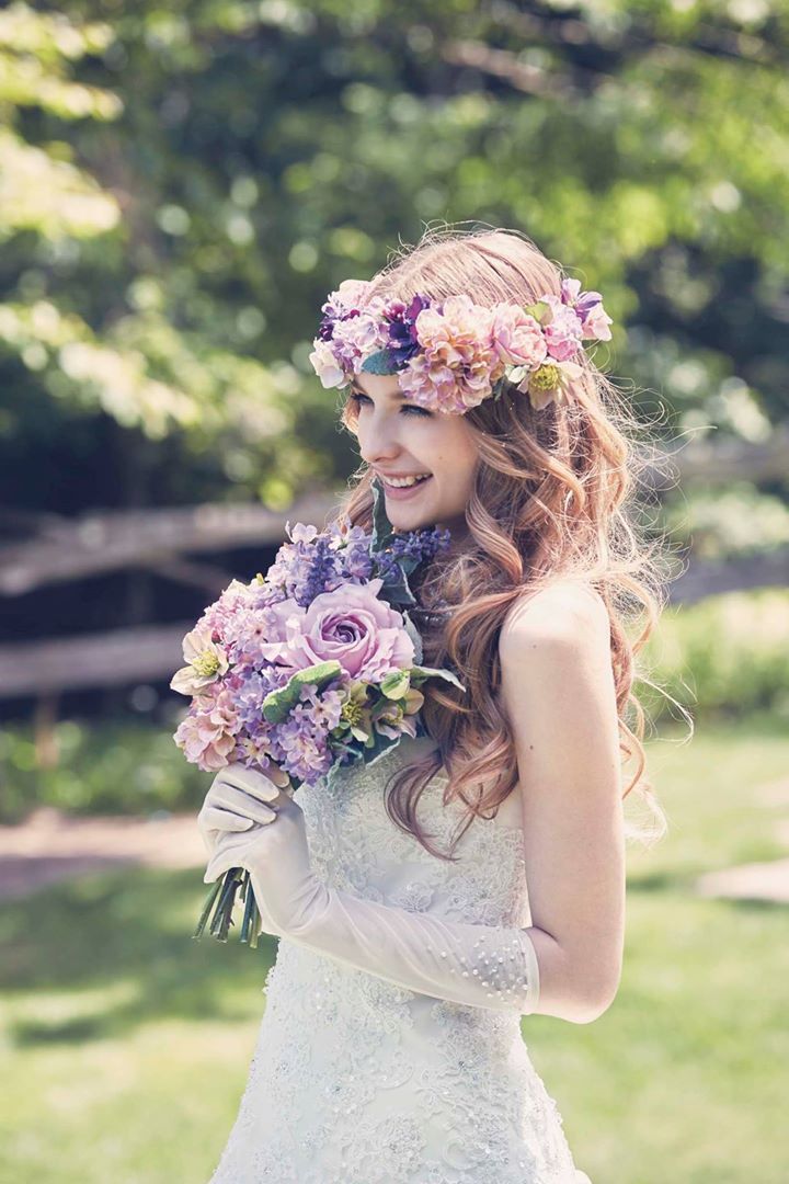 a beautiful young woman in a wedding dress with flowers on her head holding a bouquet