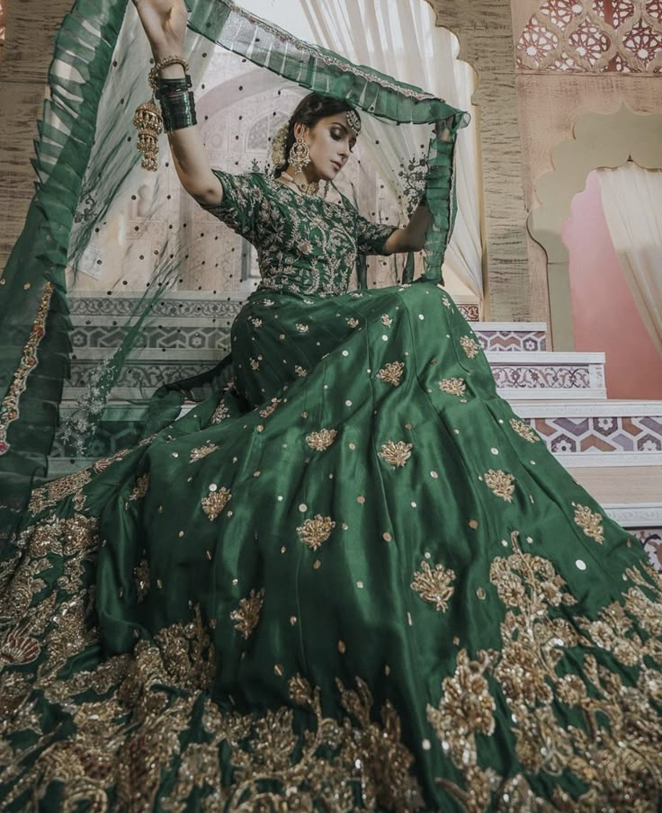 a woman in a green and gold wedding dress sitting on a bed with her arms up