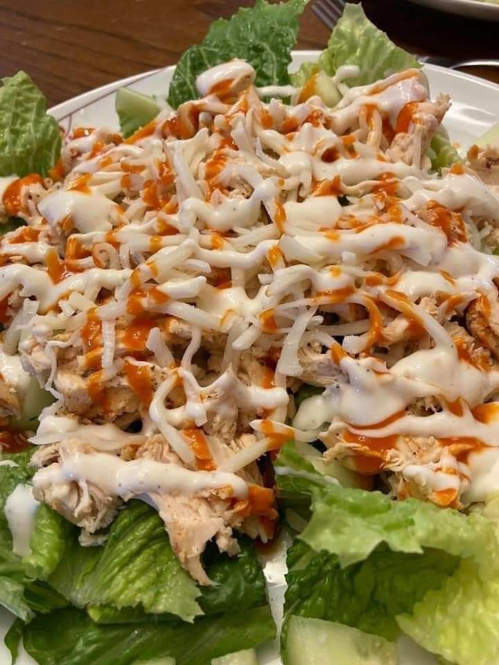 a white plate topped with lettuce and chicken salad covered in ranch dressing on top of it