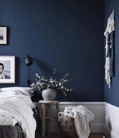 a bedroom with dark blue walls and white bedding is pictured in this image, there are pictures on the wall above the bed