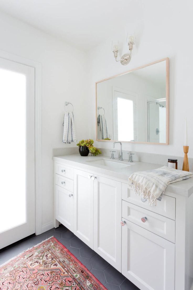 a white bathroom with a rug on the floor and a large mirror over the sink