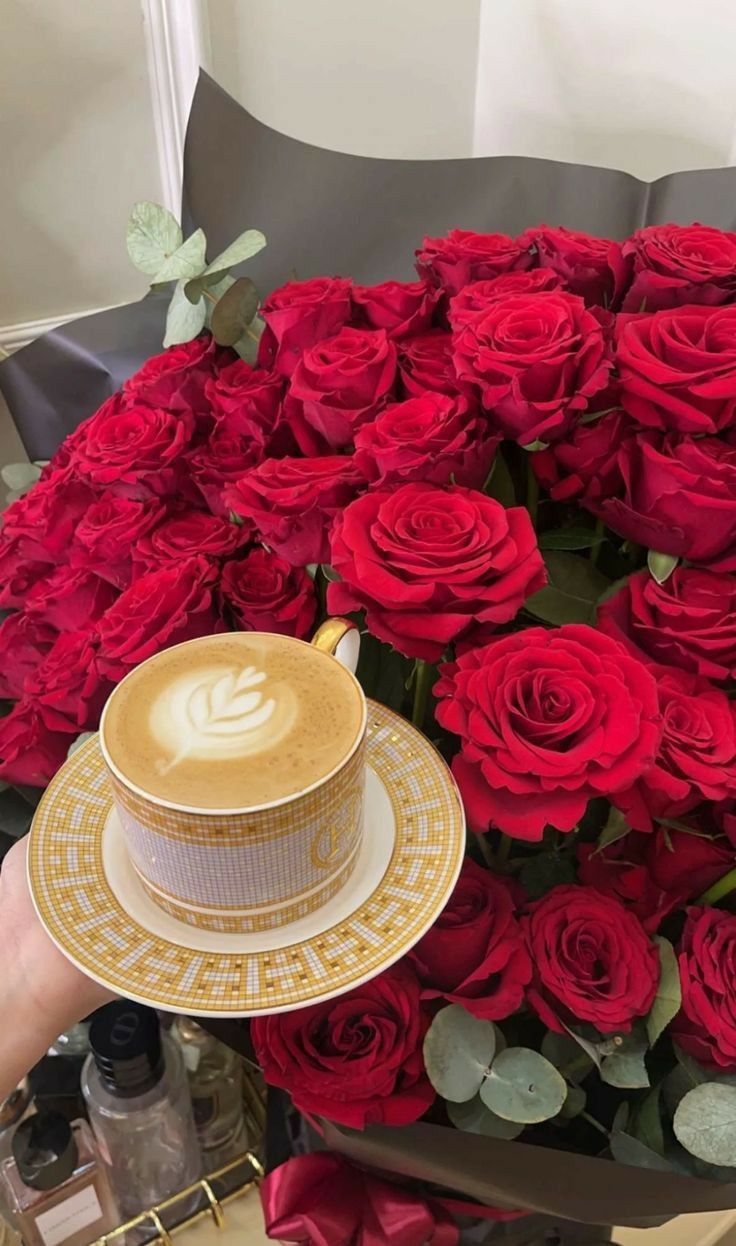 A Person Holding A Coffee Cup In Front Of A Bouquet Of Red Roses a-person-holding-a-coffee-cup-in-front-of-a-bouquet-of-red-roses