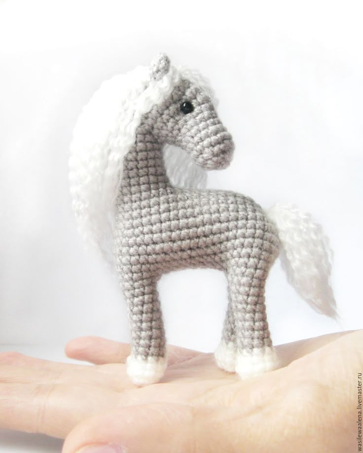 a small crocheted toy horse sitting on top of someone's hand in front of a white background