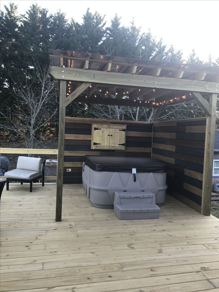 an outdoor hot tub on a wooden deck with lights strung above it and two