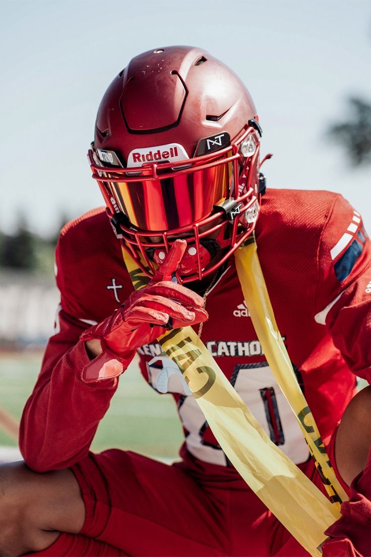 a football player wearing a red uniform and holding a yellow bat in his hand while sitting on the field