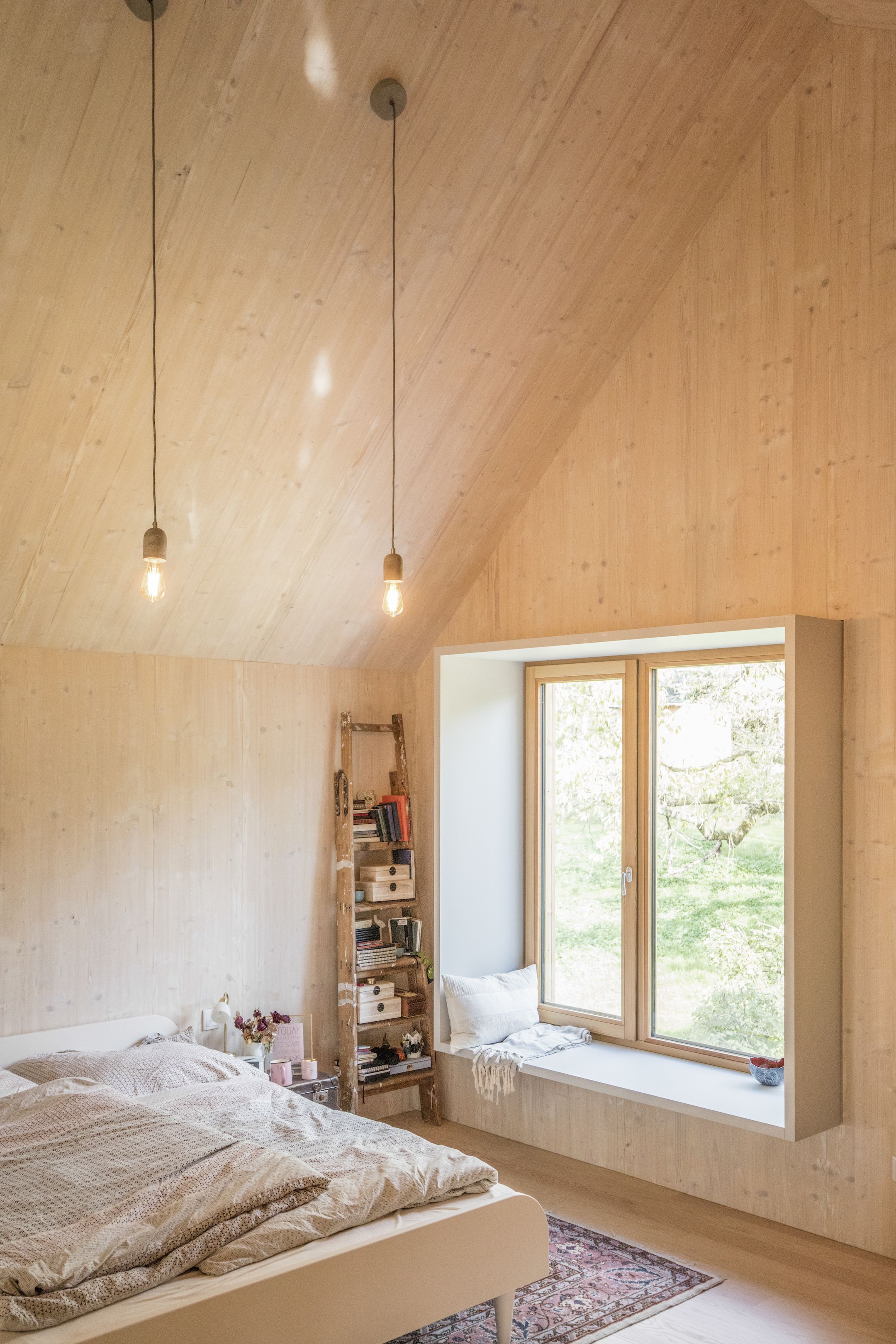 The sloped ceiling adds a layer of romance to the quaint bedroom, lit by minimal ceiling lights designed by FIRM. A rug, owned by the clients, adds a dash of color to the ash wood room. Ceiling Light Design, Lighting Design, Ceiling Lights, Sloped Ceiling Lighting, Sloped Ceiling Bedroom, Interior Lighting, Casa Natural, Clad Home, Plywood Interior