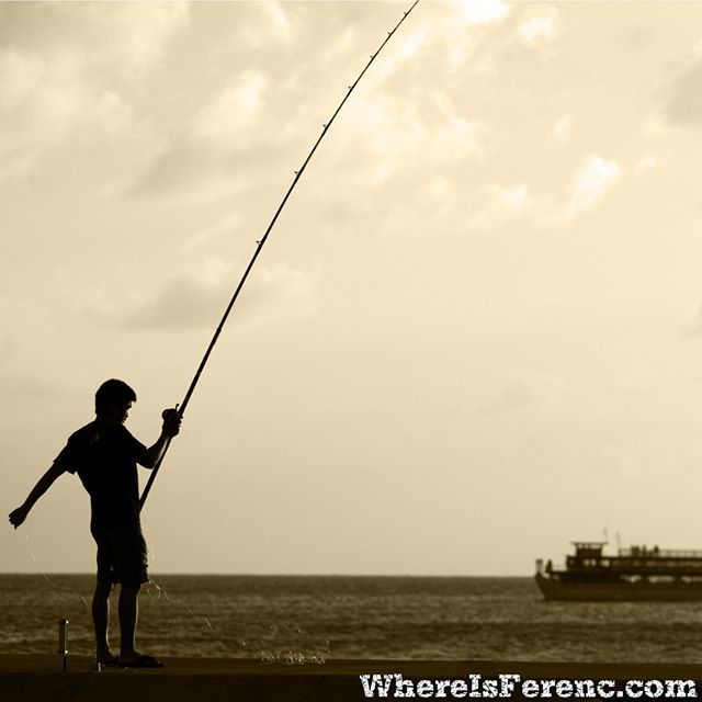 The Juxtaposition Of Fishing Man And Roaching Boat The Juxtaposition Of Fishing Man And Roaching Boat Creates An Interesting Visual On Waikiki