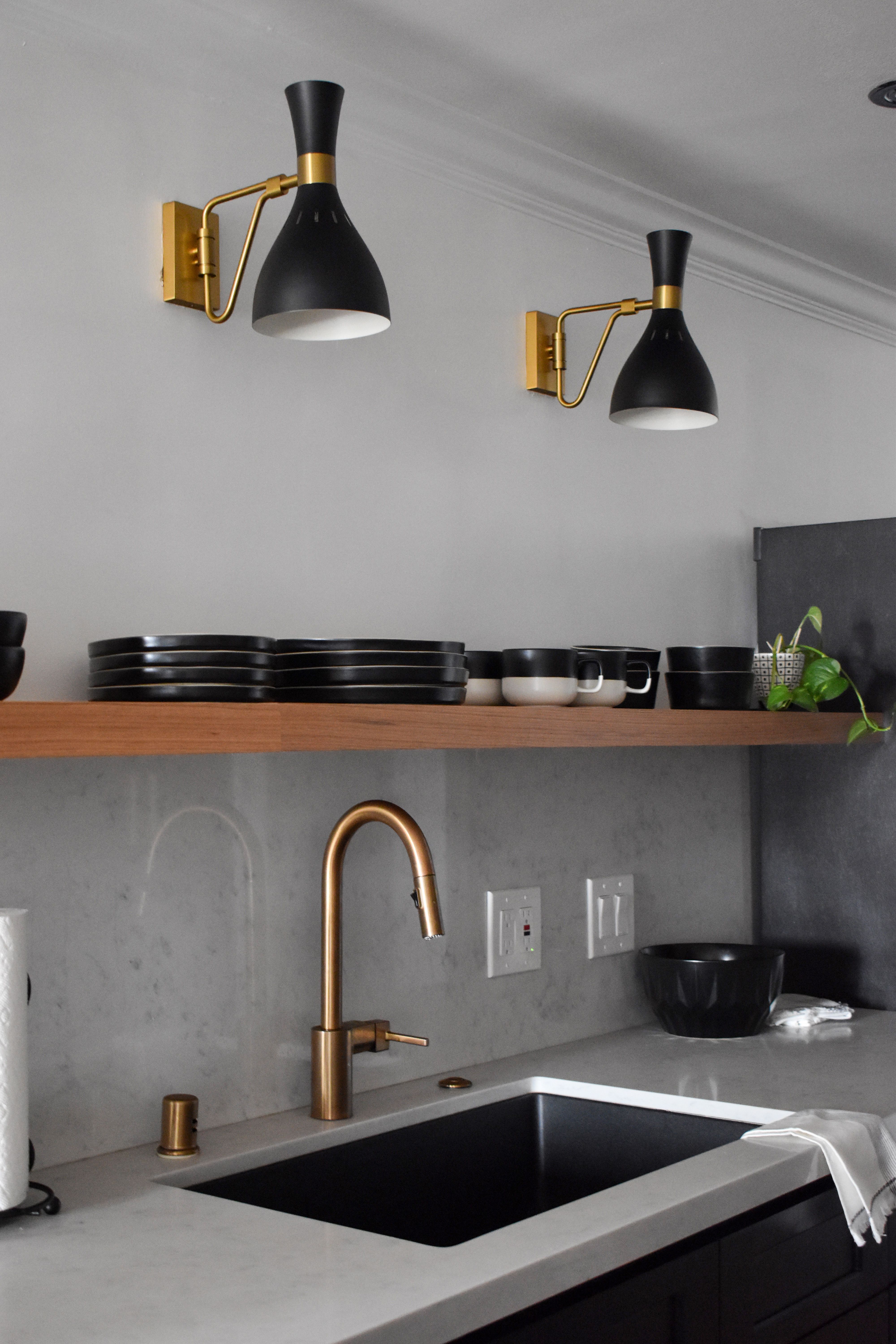 Moody boho black kitchen with brass hardware. Black and brass. Light woods. Ellen Degeneres sconces above open shelves. Black cabinets with brass cb2 drawer pulls. Brass moen sink faucet. cb2 dishes. Brass Kitchen Faucet, Kitchen Hardware, Black Kitchen Sinks, Black Sink, Kitchen Sink Lighting Ideas, Kitchen Ideas, Kitchen Design, Above Kitchen Cabinets, Above Sink Lighting Kitchen