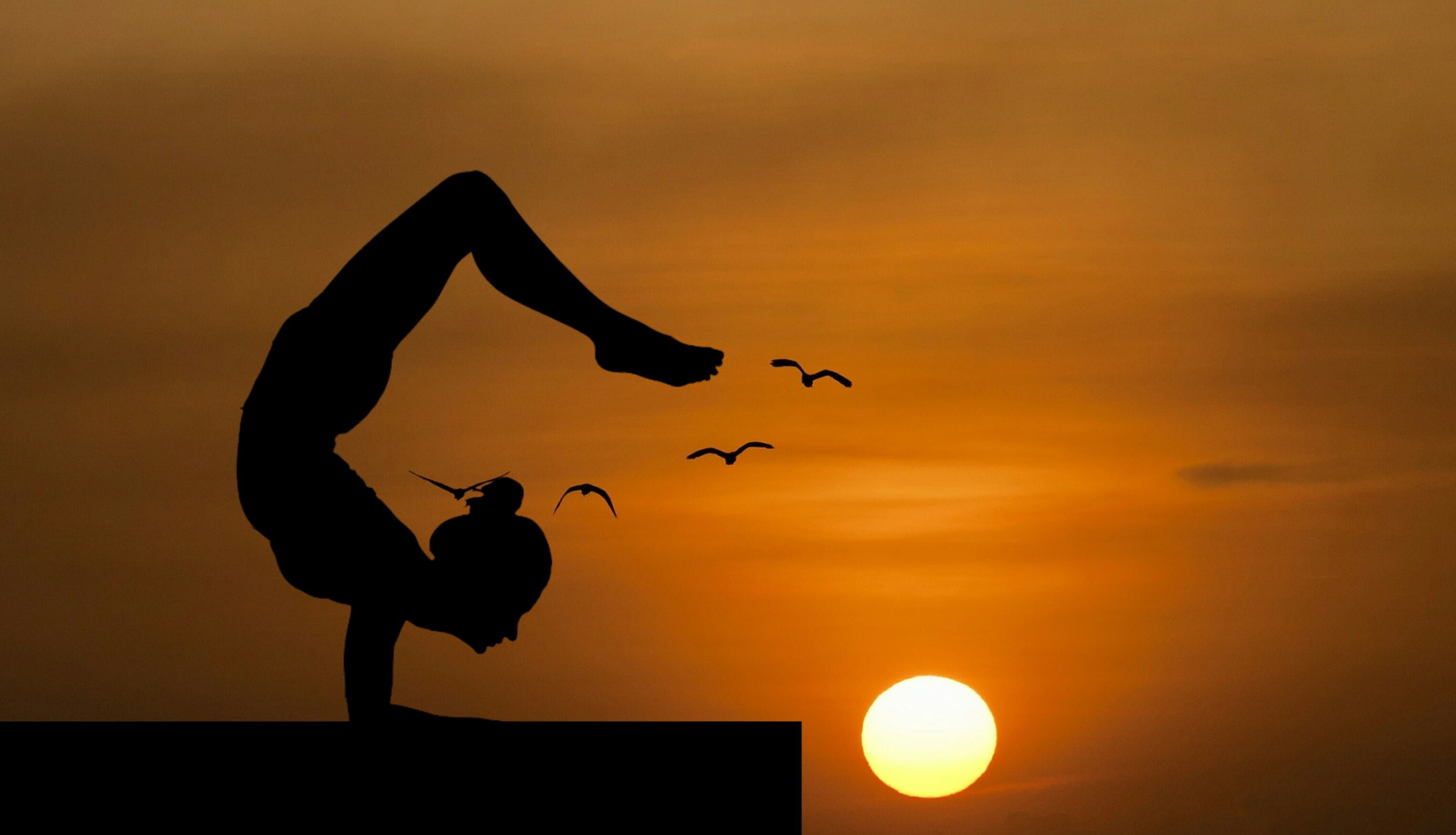 Woman doing an acrobatic yoga pose, silhouetted against sunset. #yoga #