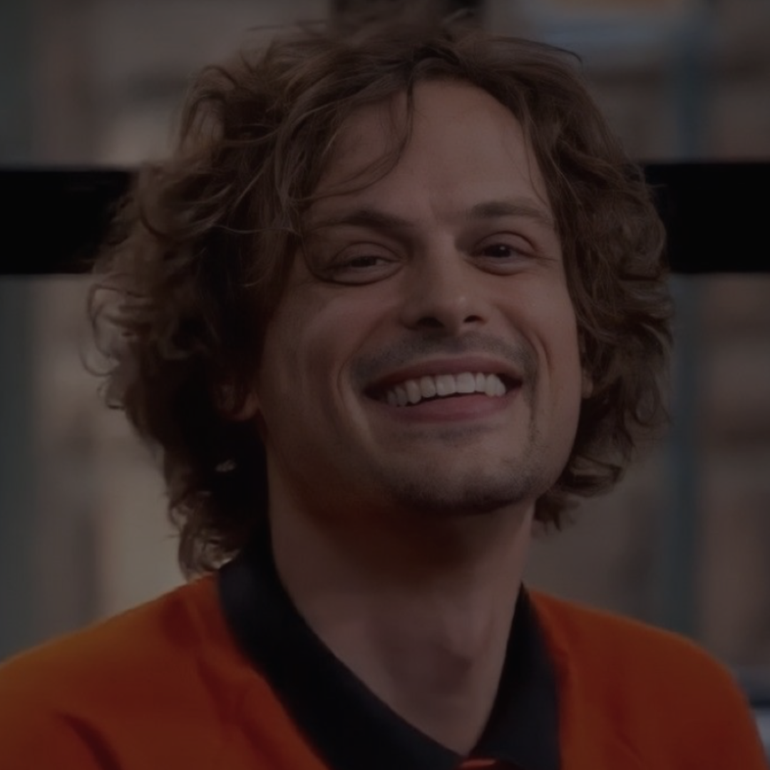 a man with curly hair smiling and wearing an orange shirt in front of a