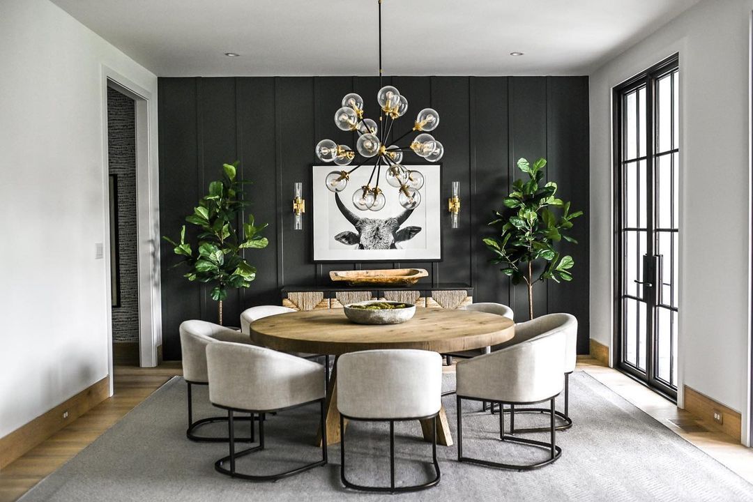 Gray and black dining chairs are seated at a round wooden dining table standing on a gray rug. Gold and glass elegant wall sconces for dining room are mounted to a black board and batten wall behind the dining set. Dining Room Interiors, Dining Room Walls, Modern Dining Room, Kitchen Dining Room, Dining Room Decor, Dining Table, Dining Room Accent Wall, Round Dining Room, Diy Dining
