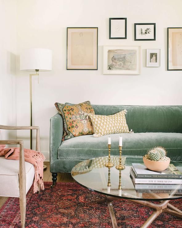A green velvet shelter back sofa sits on a red rug at a glass and wood coffee table and beneath an art gallery lit by a brass floor lamp. Living Decor, Living Room Furniture, Living Rooms, Living Room Decor Green Couch, Living Room White Walls, Green Sofa Decor, Mid Century Modern Living Room Sofas, Green Velvet Sofa Living Room, Boho Living Room Sofas