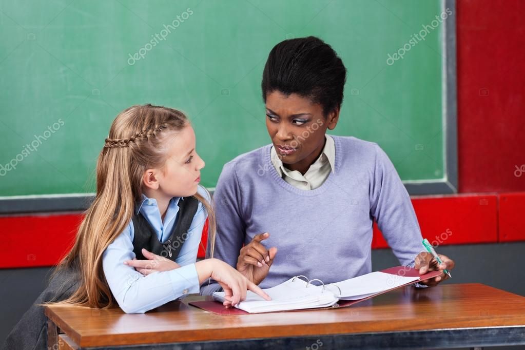 Female Teacher Looking At Schoolgirl In Classroom Royalty Free