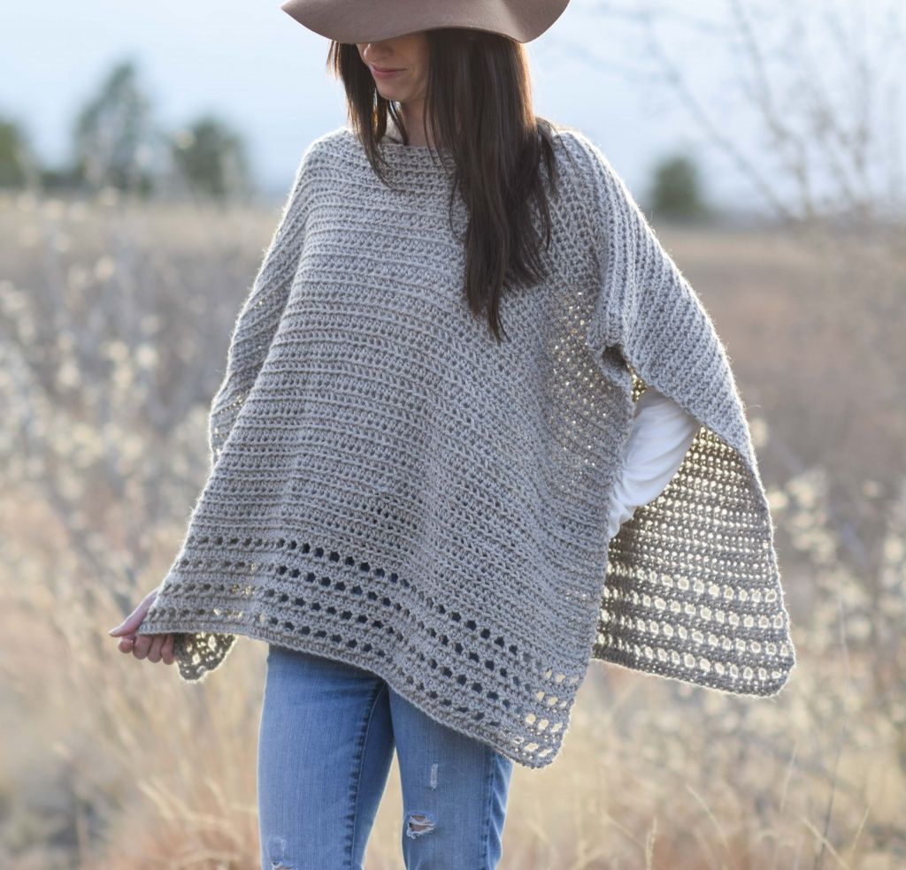 a woman wearing a crochet ponchy standing in the middle of a field