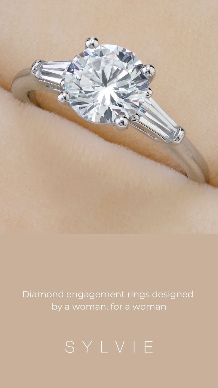 This stunning three-stone engagement ring by Sylvie features a 1.5 carat round brilliant center surrounded by two shimmering baguette diamonds on each side. The stones are set on a classic high polish shank for a traditional and practical look that never goes out of style. Tap here to learn more. (Style Shown: Nicolette S3012) #SomethingSYLVIE #EngagementRings #DiamondRings #WeddingRings #DiamondRing #BaguetteEngagementRings #DesignerEngagementRings #CustomEngagementRings Three Stone Engagement Rings, Custom Engagement Ring, Three Stone Rings, Designer Engagement Rings, Types Of Gold, Thing 1, Baguette Diamond, Out Of Style, Princess Cut