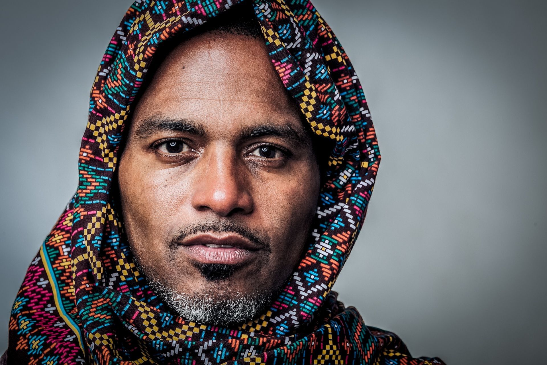 a man with a colorful scarf on his head looking at the camera while wearing a hoodie