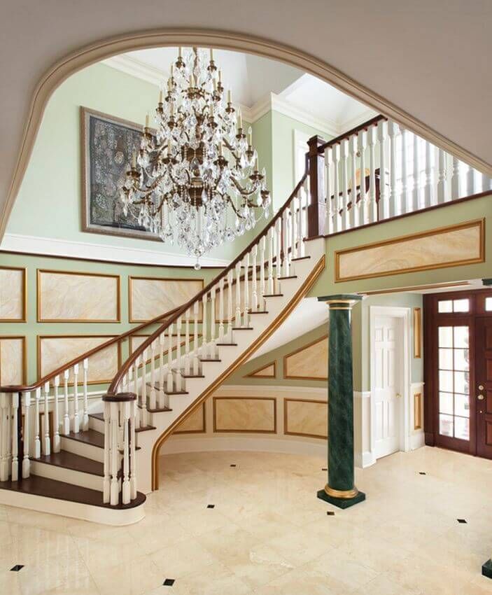 An incredible ornate foyer with a curving staircase green marble columns and a wealth