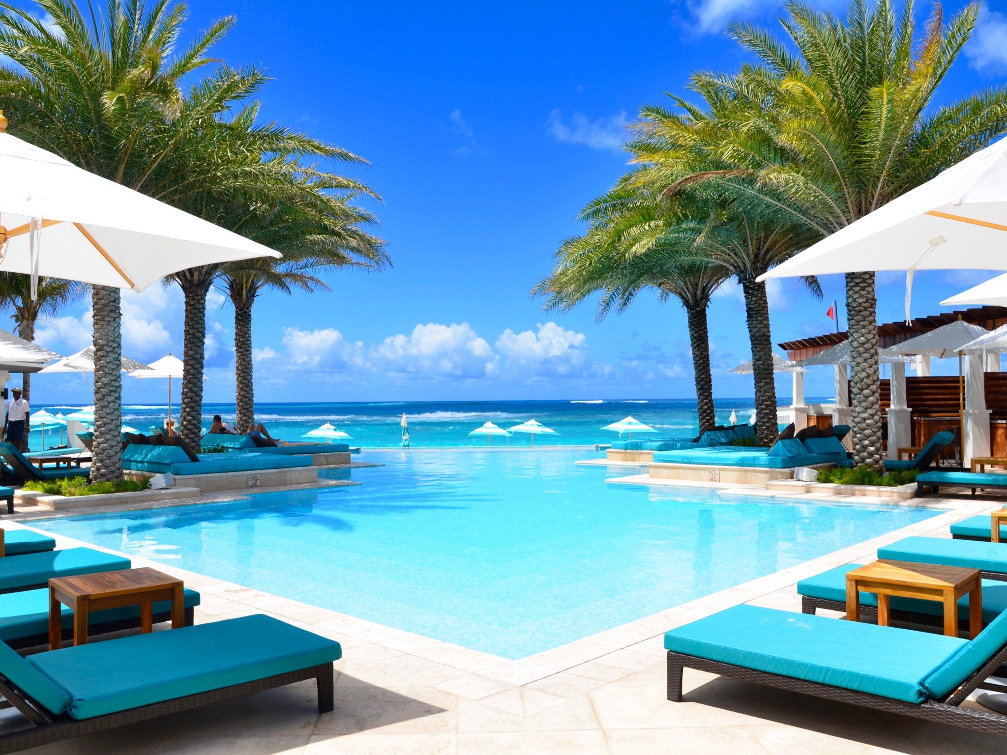 An Outdoor Pool With Chaise Lounges And Umbrellas Next To The Ocean On 